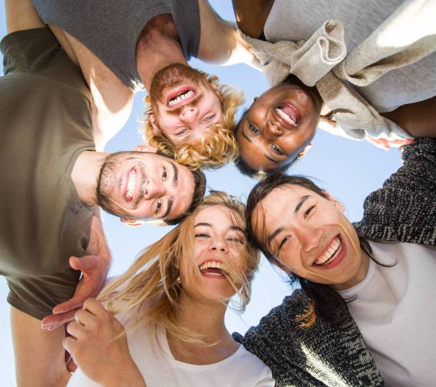 Cheerful friends huddling against blue sky on sunny day